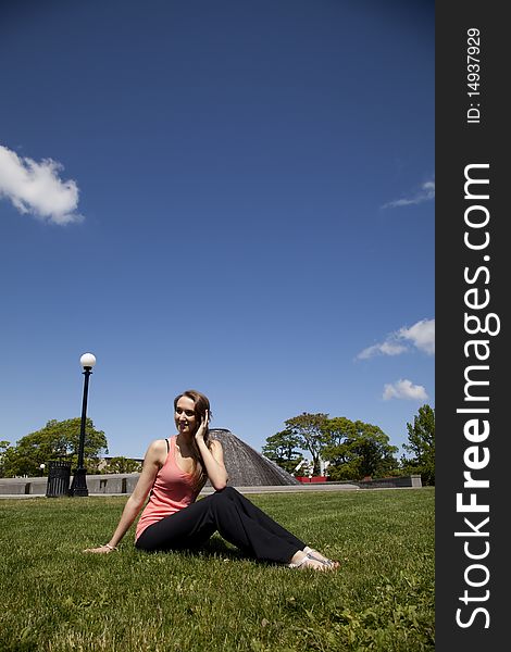 A woman sitting on the grass at the park looking at something with a small smile on her face. A woman sitting on the grass at the park looking at something with a small smile on her face.