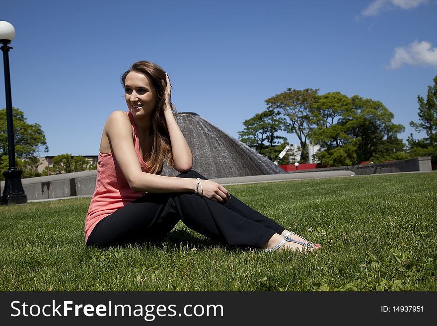 A woman playing with her hair while she is sitting on the grass on a beautiful day in the park. A woman playing with her hair while she is sitting on the grass on a beautiful day in the park.