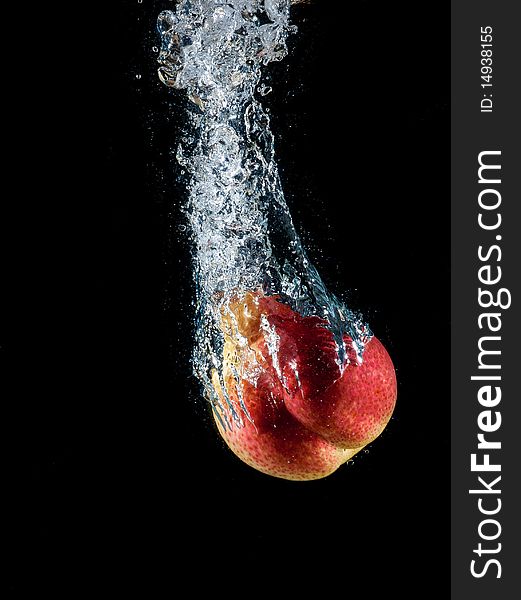 Image of a red ripe pear dropped into water on black background
