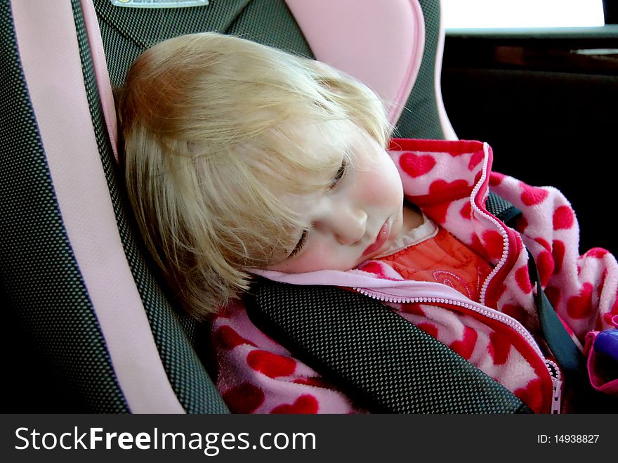 A sad little girl is travelling in a car seat fastened with safety belts. A sad little girl is travelling in a car seat fastened with safety belts