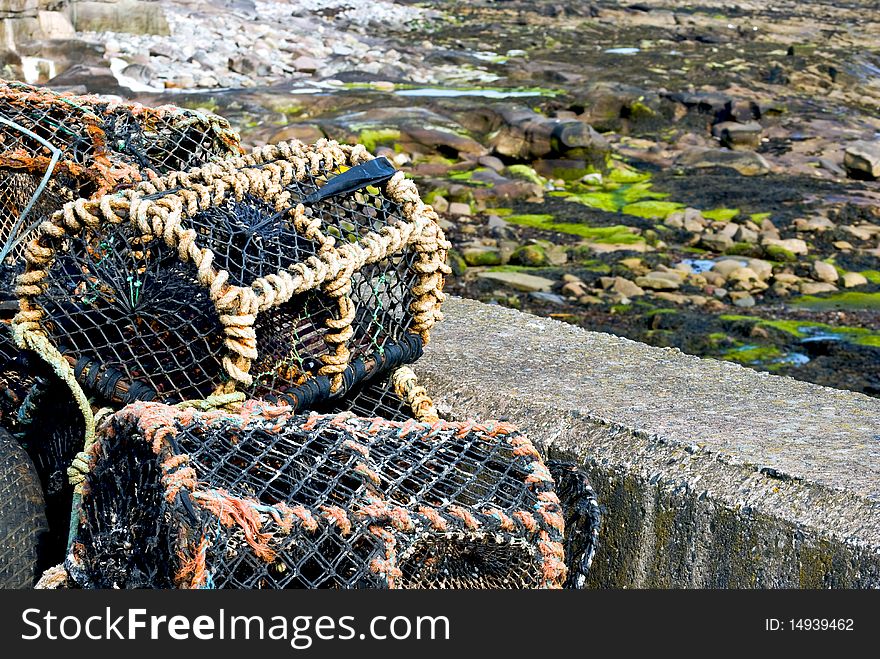A stack of crab traps at the harbour with the sea at low tide in the background