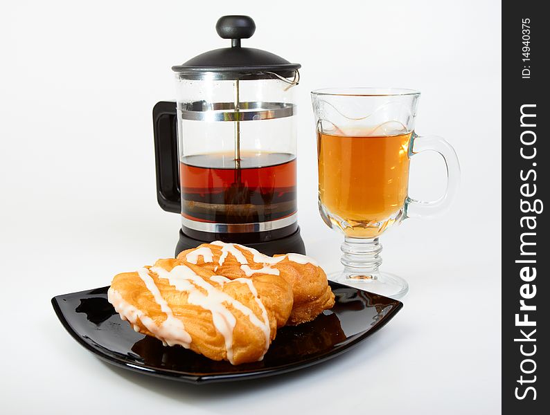 Two pastries filled with custard on black plate with teapot and cup of tea on white background. Two pastries filled with custard on black plate with teapot and cup of tea on white background