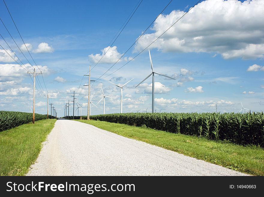 Electric power lines and wind mills run parallel along side a country road. Electric power lines and wind mills run parallel along side a country road.