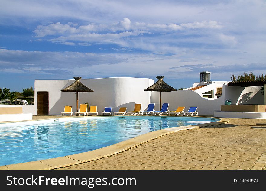 Swimming pool with lounge chairs and thatched umbrellas. Swimming pool with lounge chairs and thatched umbrellas