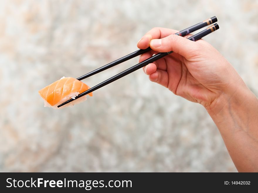 Holding a piece of salmon sushi with chopsticks