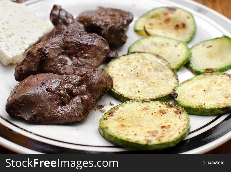 Slices of green and yellow Italian zucchini, pan fried and sprinkled with herbs. Served on white plate with chicken liver. Slices of green and yellow Italian zucchini, pan fried and sprinkled with herbs. Served on white plate with chicken liver.