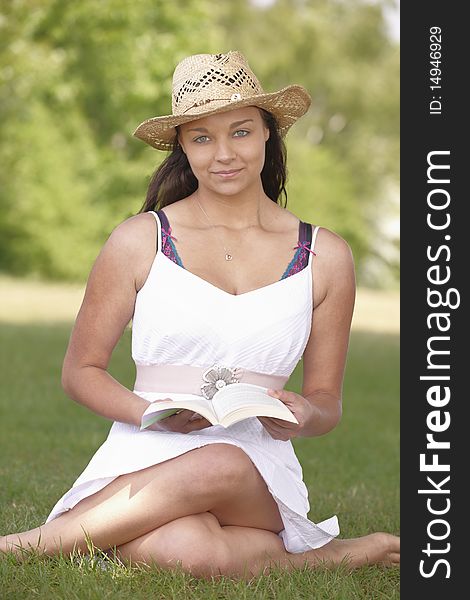 Young attractive girl sitting on grass while reading a book. Young attractive girl sitting on grass while reading a book