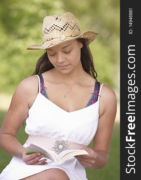 Young attractive girl sitting on grass while reading a book. Young attractive girl sitting on grass while reading a book