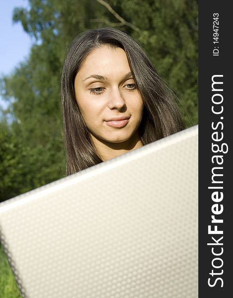Young Caucasian woman with a laptop in the park on a green grass / meadow