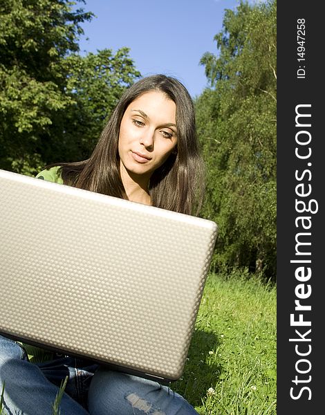 Young Caucasian woman with a laptop in the park on a green grass / meadow