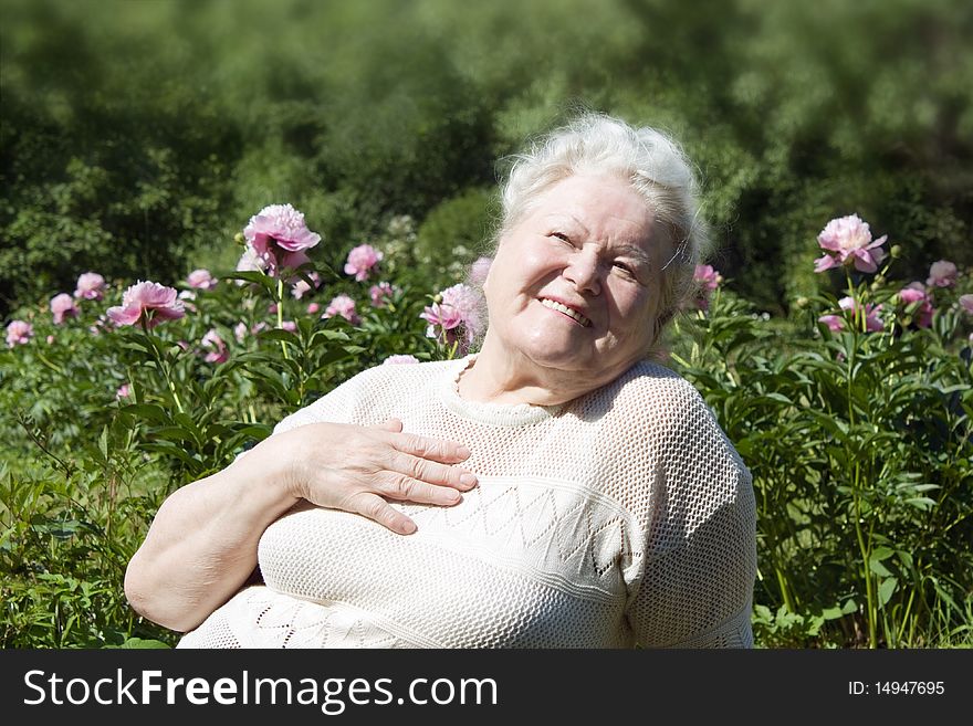 Senior woman enjoying the summer garden and sunlight, focus on foreground.