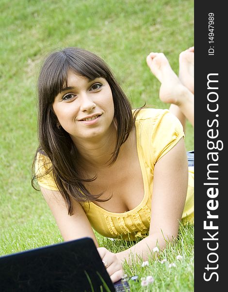 Young Caucasian woman with a laptop in the park on a green grass / meadow