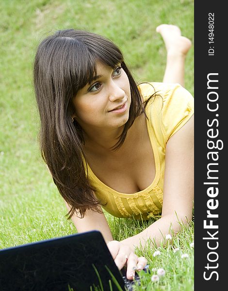 Young Caucasian woman with a laptop in the park on a green grass / meadow