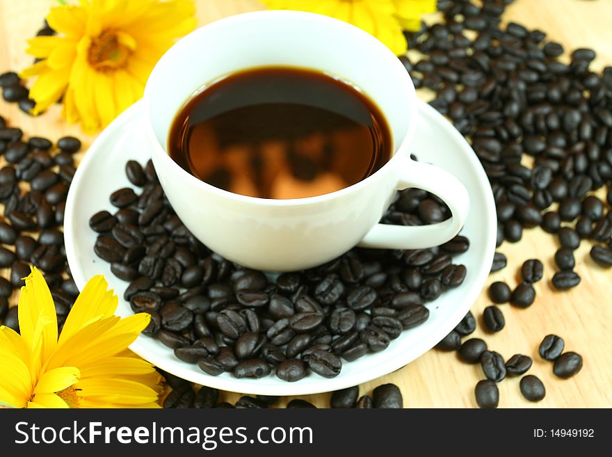 Black coffee with reflection in white cup. Beans and yellow flowers. Black coffee with reflection in white cup. Beans and yellow flowers
