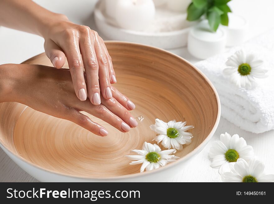 Woman soaking her hands in bowl of water and flowers on table, closeup. Spa treatment