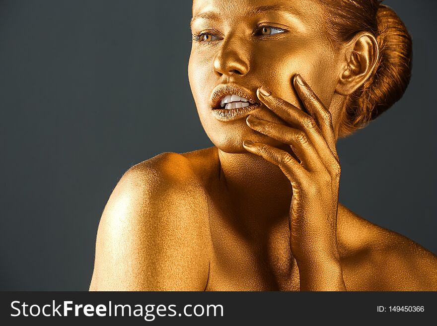 Portrait of beautiful lady with gold paint on skin against grey background, closeup