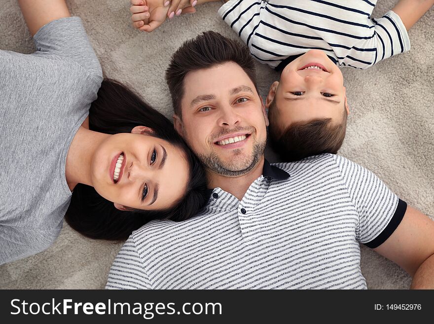 Happy parents and their son lying together on floor, view from above. Family time. Happy parents and their son lying together on floor, view from above. Family time