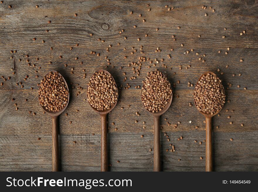 Spoons with uncooked buckwheat on wooden table, flat lay. Space for text