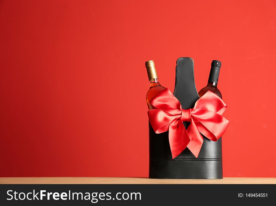 Bottles of wine in holder with bow on table against color background