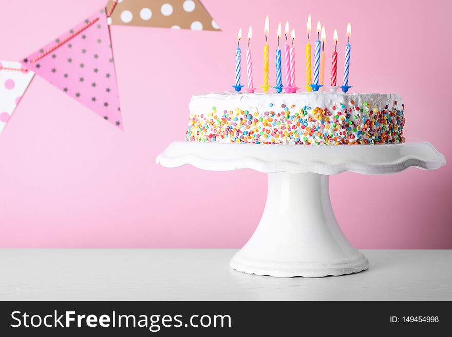 Birthday cake with burning candles on table against color background. Space for text