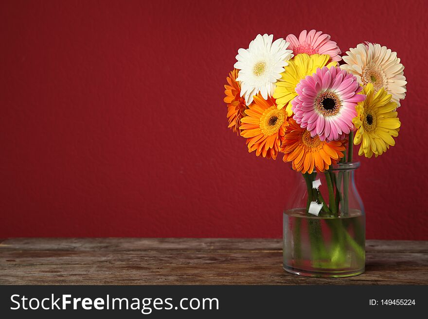 Bouquet of beautiful bright gerbera flowers in vase on wooden table against color background. Space for text