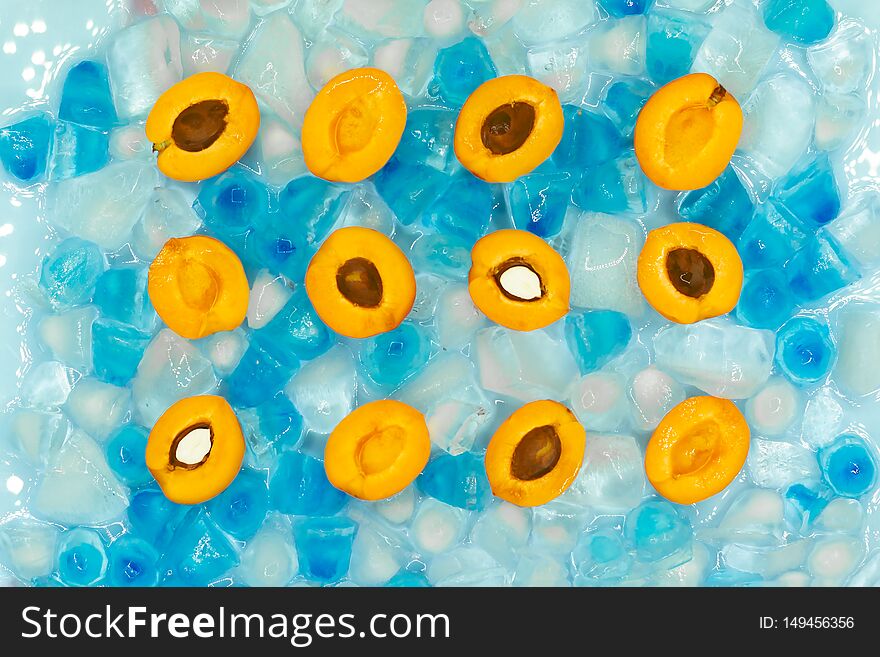 Cut halves of ripe apricots with or without stones against the background of transparent and blue ice cubes. Fresh summer pattern. Top view