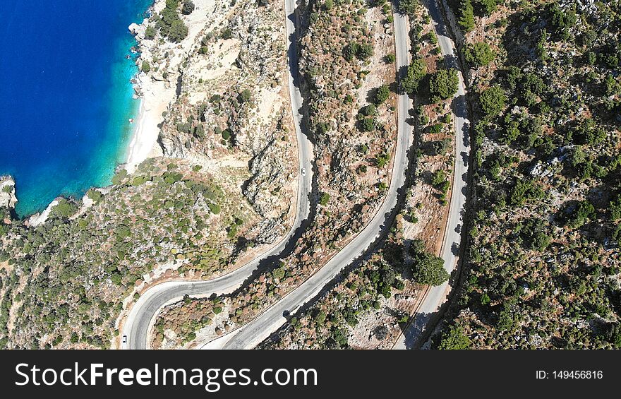 Aerial serpentine road. Traffic motion on a highway road in the mountains by the sea. Trip by car. Top view.