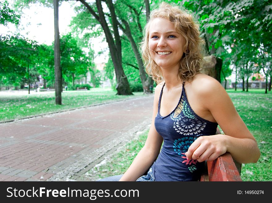 Young beautiful girl sitting on a park bench and smiles. Young beautiful girl sitting on a park bench and smiles.