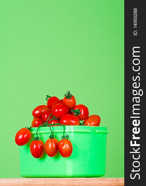 Container with fresh tomatoes on green background