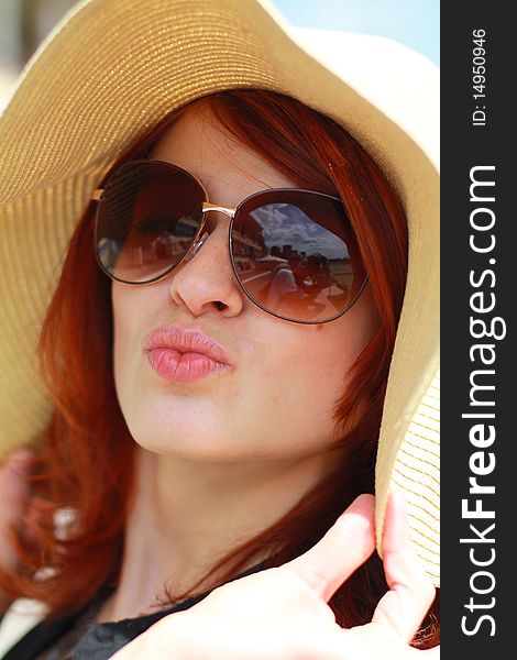 Pretty red-haired girl in hat and sunglasses blows a kiss