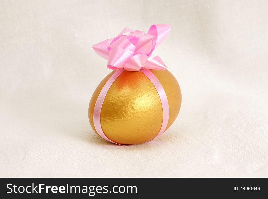 A golden egg wrapped in pink ribbon with a white fabric as background