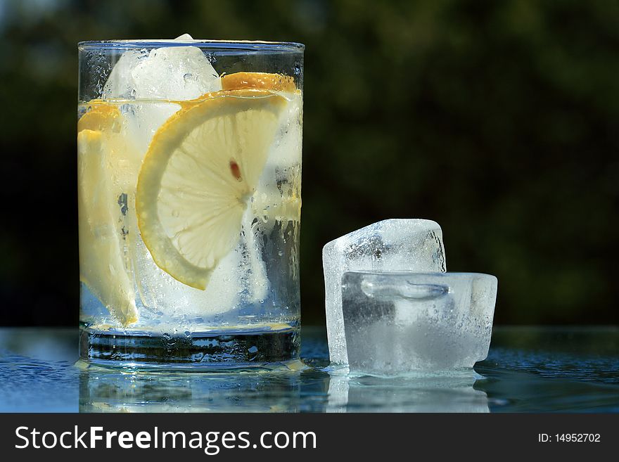 Glass of cold lemonade and ice cubes on dark background with copy space. Glass of cold lemonade and ice cubes on dark background with copy space