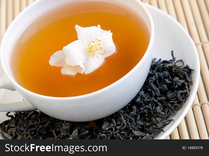 A cup of tea on a tray with dried tea and jasmine flower. A cup of tea on a tray with dried tea and jasmine flower