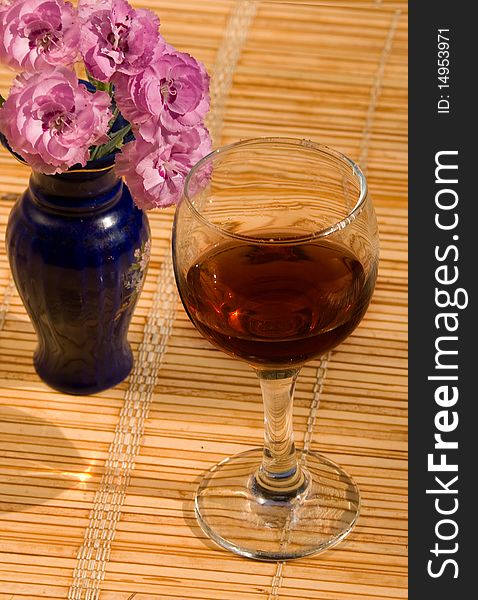 Glass of a brandy and pink carnations on a straw napkin