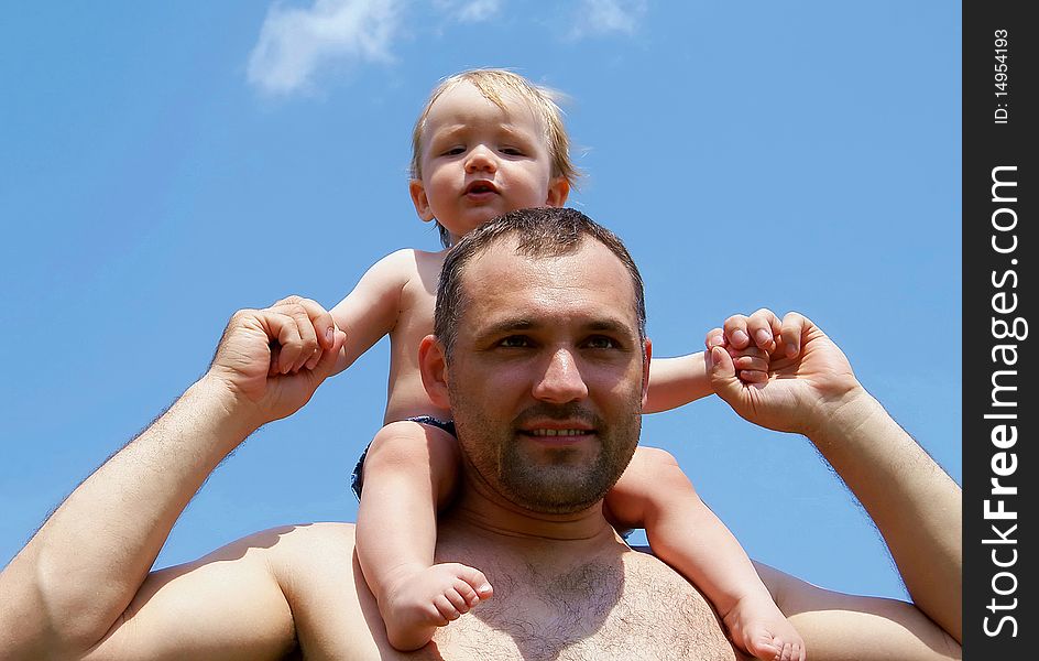 In the summer against the sky the man holds the kid for hands having put to itself on shoulders. In the summer against the sky the man holds the kid for hands having put to itself on shoulders