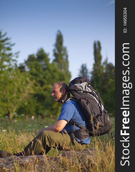 Backpacker / hiker sitting on a rock in a field on a sunny evening. Backpacker / hiker sitting on a rock in a field on a sunny evening