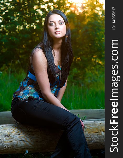 Young woman sitting on a log, summer colors, sunlight, nature