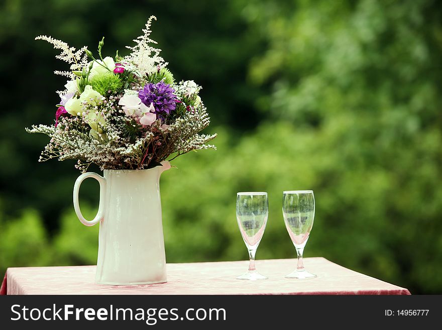 Fine bouquet made of different flowers and with two wine glasses on a table. Fine bouquet made of different flowers and with two wine glasses on a table.