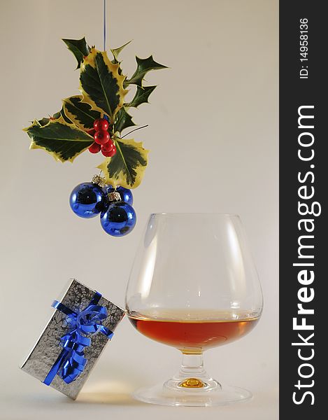 Brandy snifter with silver present under holly with red berried and blue bulbs. Brandy snifter with silver present under holly with red berried and blue bulbs