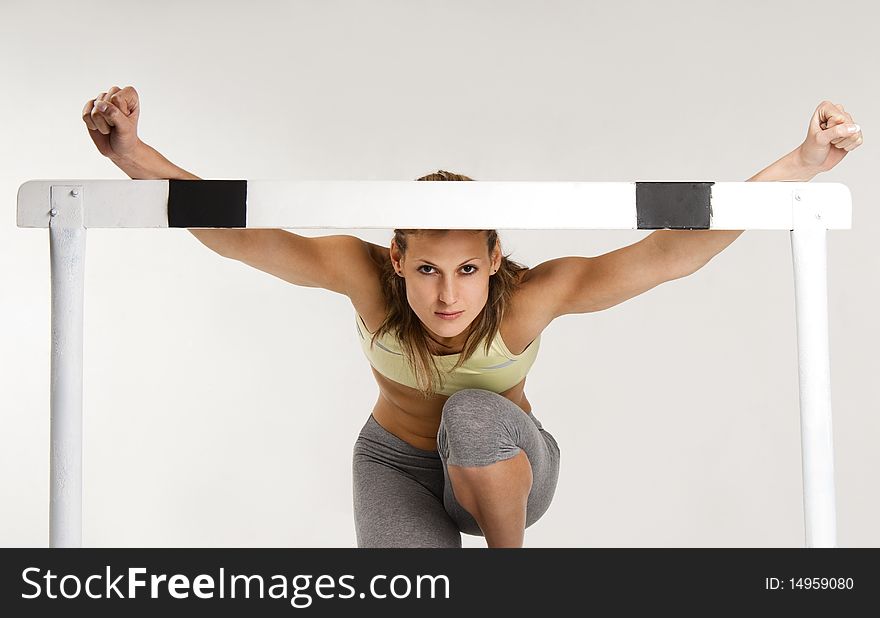 Pritty caucasian sportive model with hurdle, over gray background