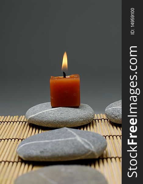 A light candle and row of stones on mat. A light candle and row of stones on mat