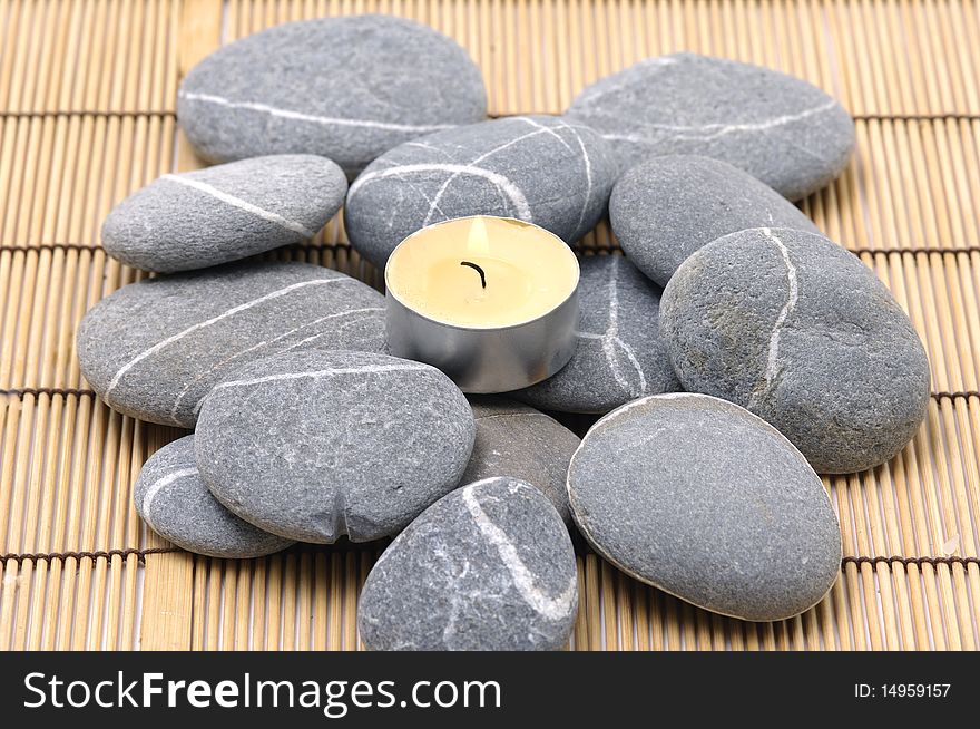 A light candle and pebbles on bamboo mat. A light candle and pebbles on bamboo mat