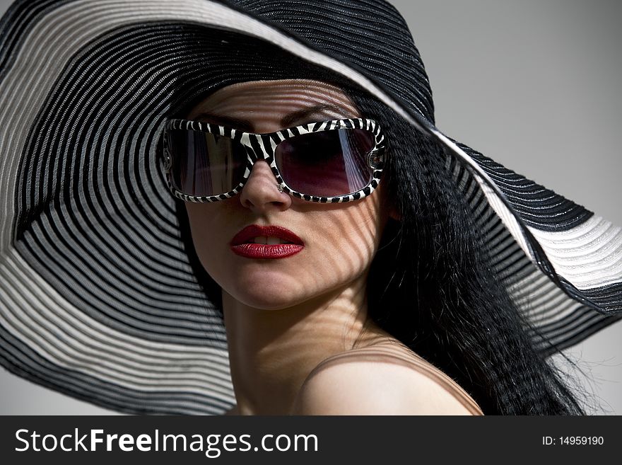 Beautiful model in striped hat and top with glassses on the gray  background