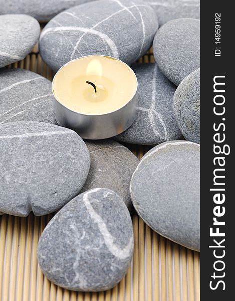 A light candle and pebbles on bamboo mat. A light candle and pebbles on bamboo mat