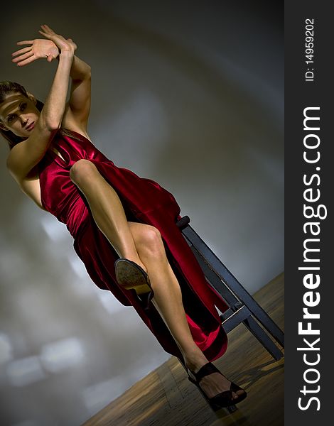 Attractive woman in red dress sit on the chair closing from blinding rays of light