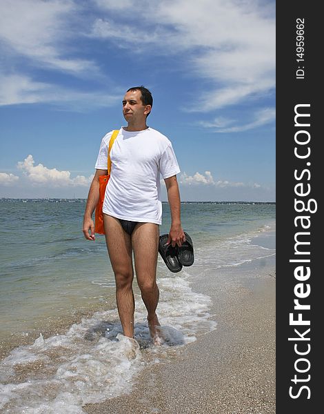 A man in a white sport shirt goes for a walk on a beach. A man in a white sport shirt goes for a walk on a beach