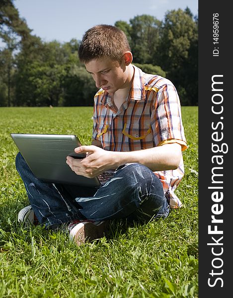 Young man sitting on green grass in park and types on laptop. Young man sitting on green grass in park and types on laptop