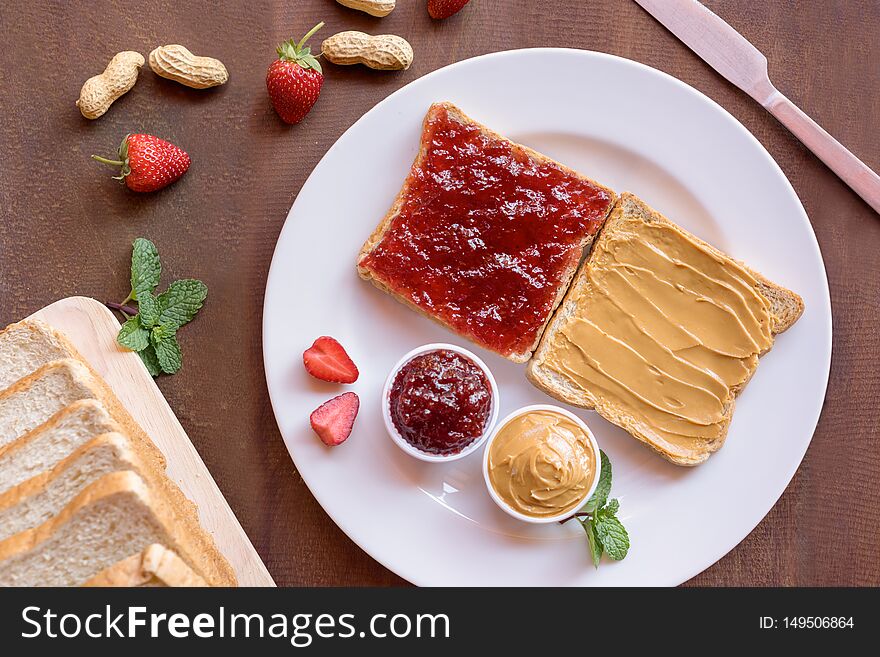 Creamy peanut butter toast and strawberry jam toast on plate with nut and fruit. Top view