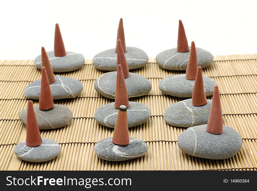 A row of incense cones over pebbles on bamboo mat. A row of incense cones over pebbles on bamboo mat