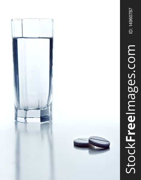 Two tablets and glass of water on white background. Two tablets and glass of water on white background